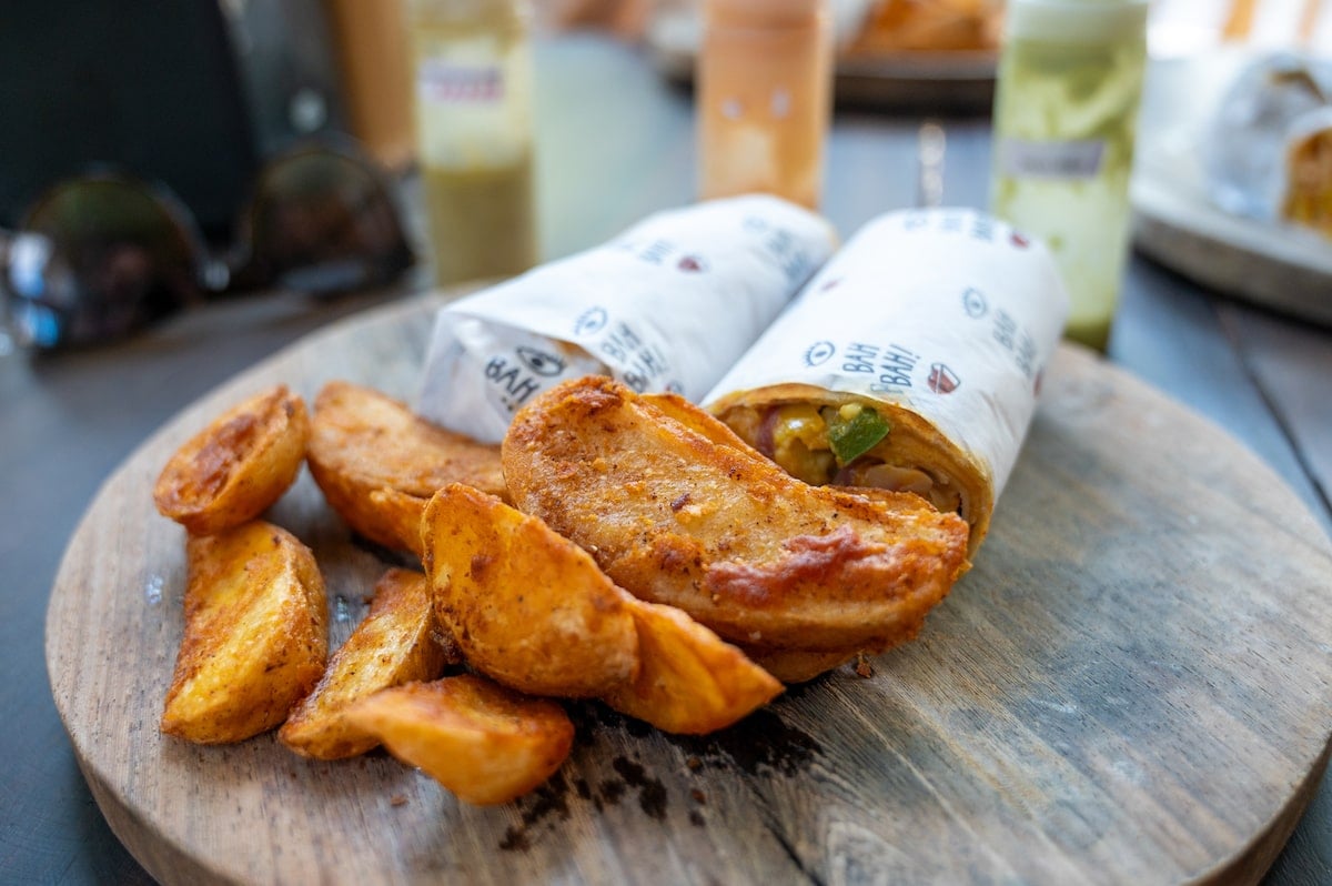 Close-up of a shrimp burrito wrapped in branded paper, served with a side of crispy rosemary potato wedges on a wooden platter at Bah Bah! Holbox Restaurante.